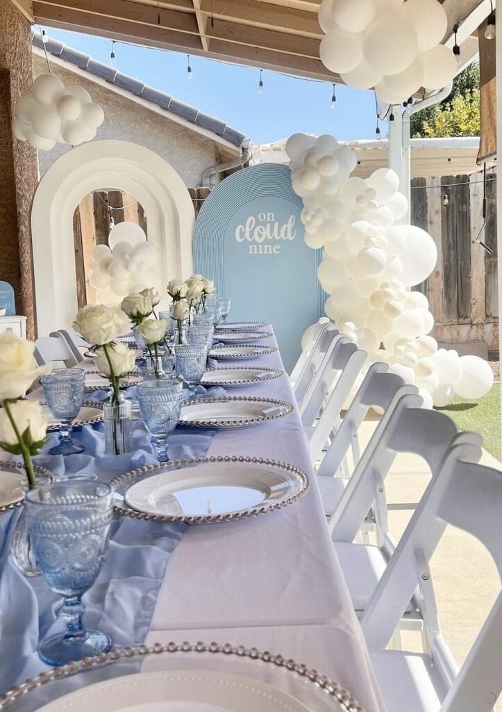 Elegant outdoor birthday celebration with white roses and cloud-themed decor.