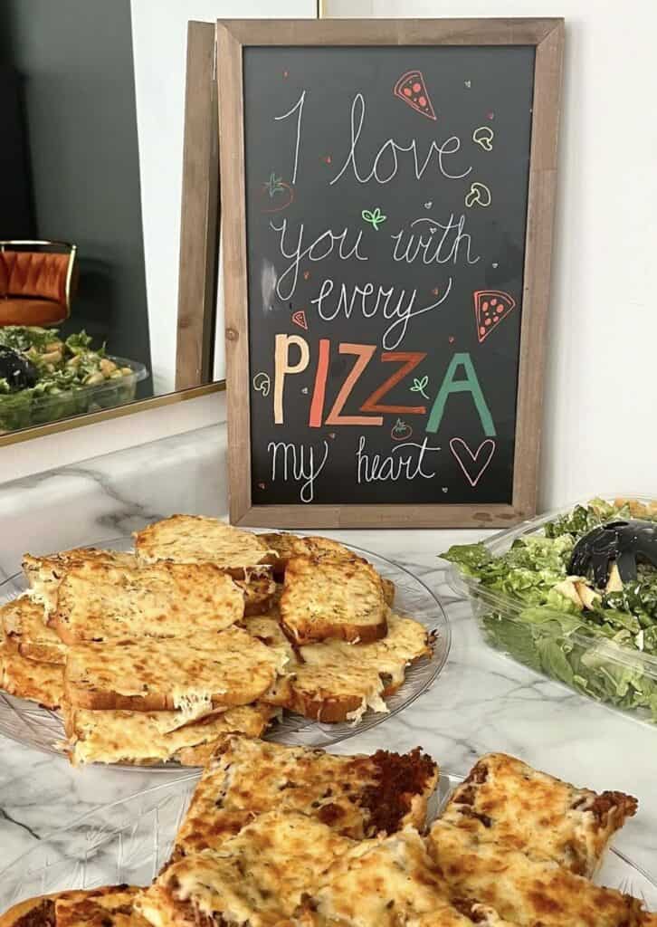 Colorful chalkboard sign with pizza and salad at Confetti & Roses, wedding catering setup.
