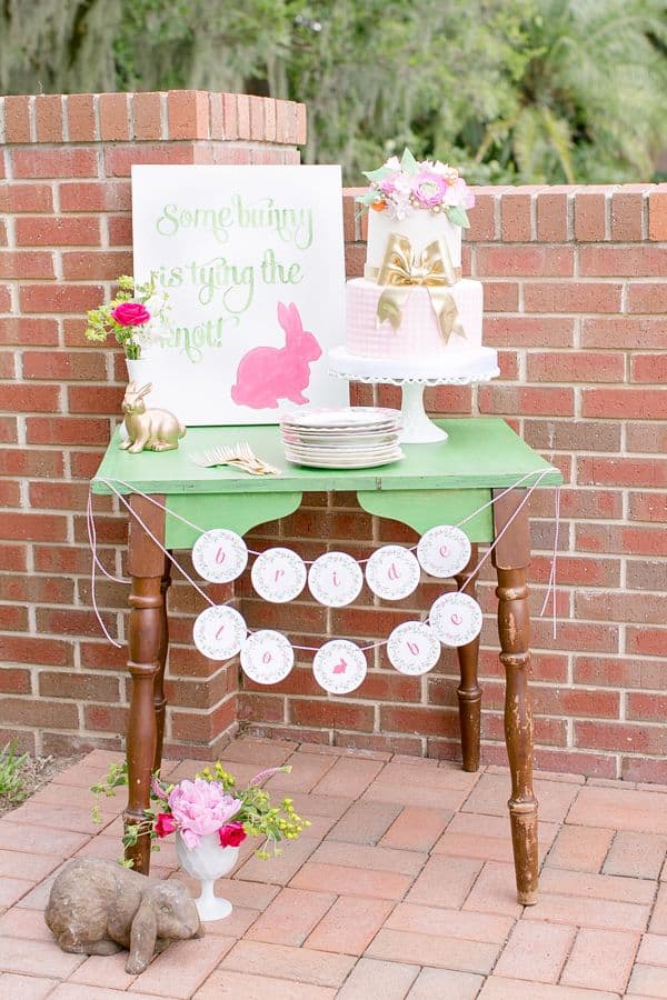 Pastel pink and green bunny-themed birthday dessert table with cake and decorations.