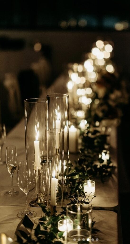 Elegant candlelit wedding table decor with tall glass candle holders and greenery.