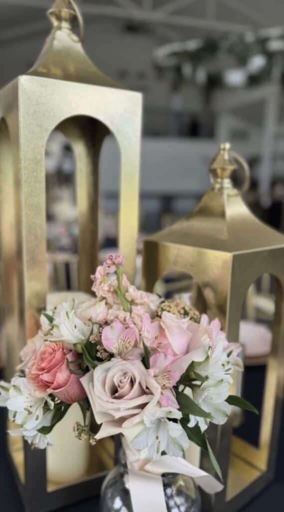 Gold lanterns with pink and white floral arrangement for wedding decor.