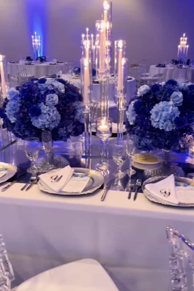 Elegant wedding table setting with blue floral centerpieces and candlelit candelabras.