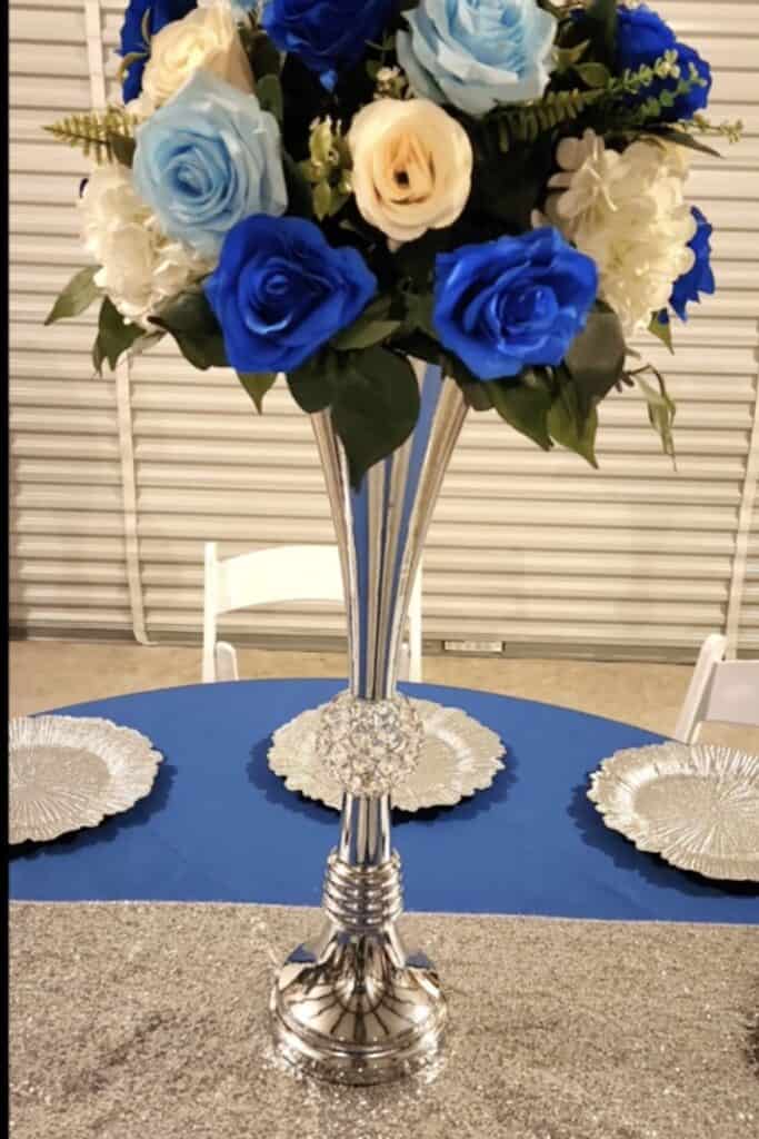 Vase with blue, cream, and white roses floral centerpiece at event table.