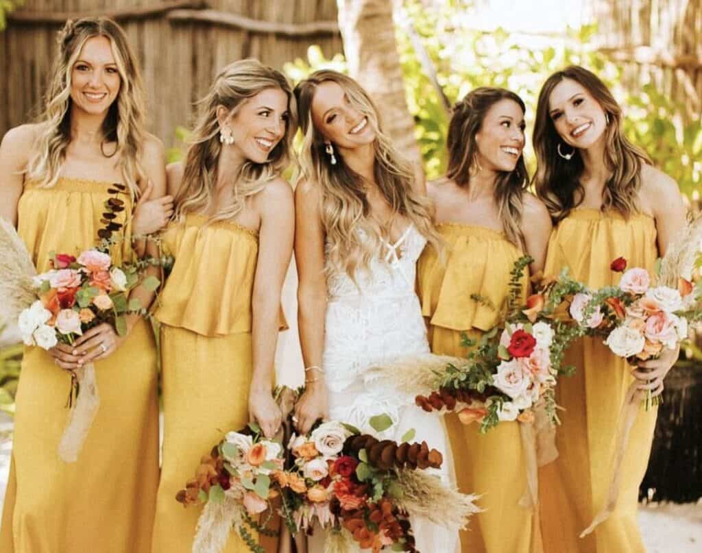 Bridesmaids in yellow dresses holding floral bouquets at outdoor wedding event.