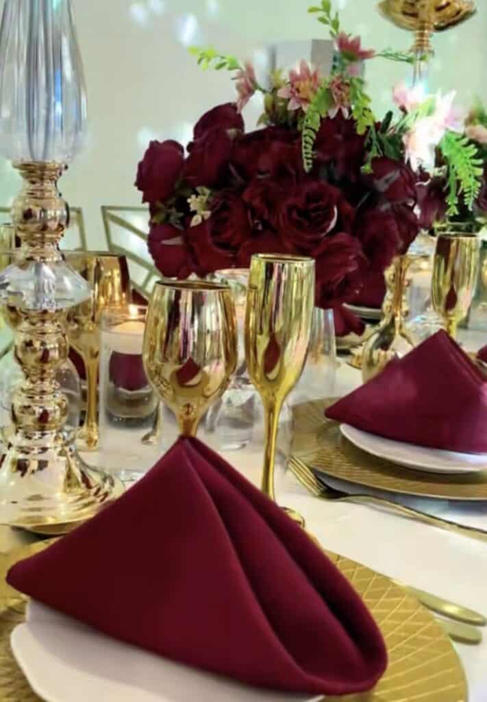 Elegant table setting with deep red roses, gold accents, and burgundy napkins.