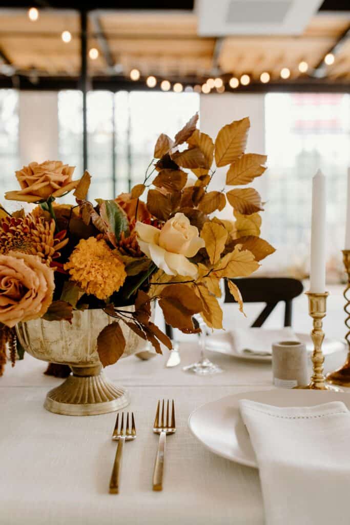 Elegant fall floral centerpiece with roses, dahlias, and autumn leaves at event table.