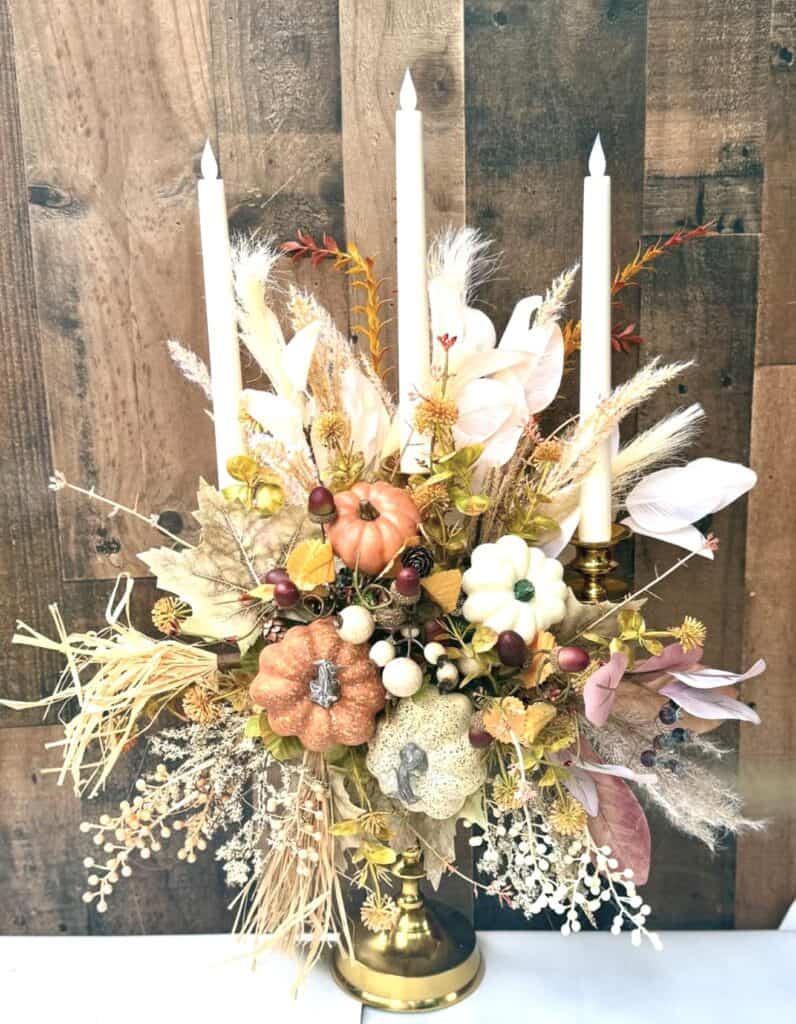 Elegant fall floral centerpiece with pumpkins and candles for wedding decor.