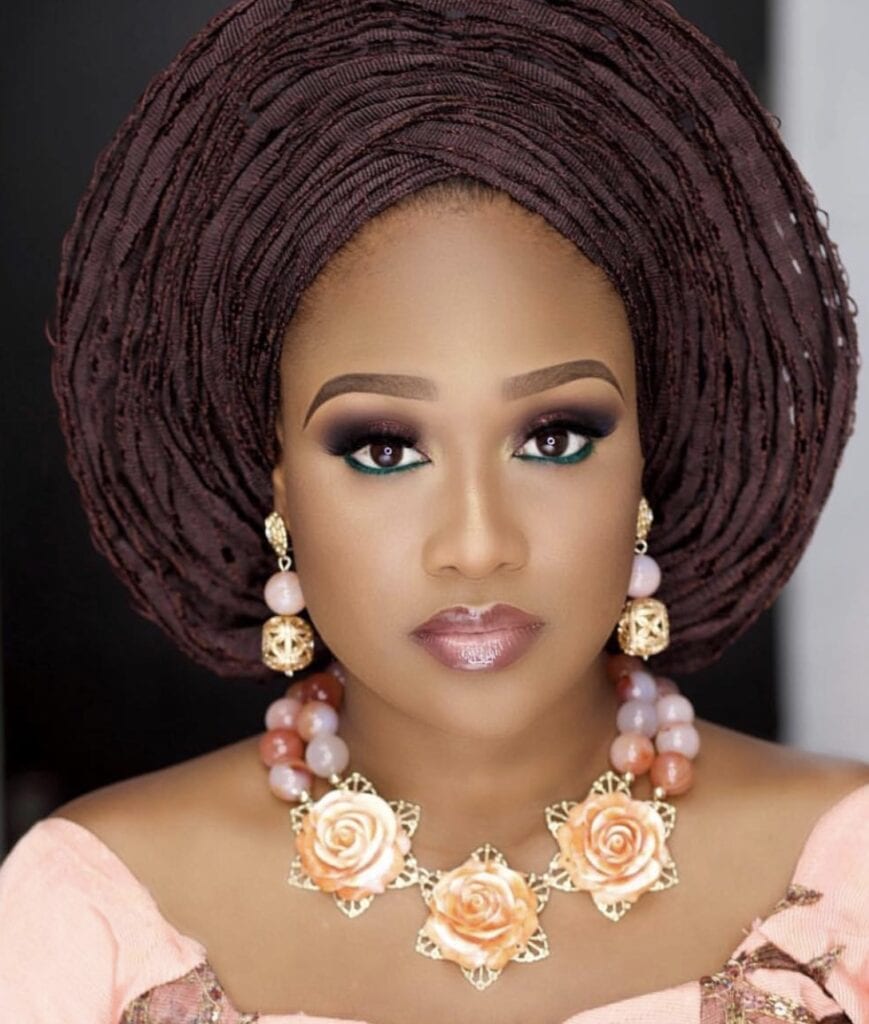 Vibrant woman with elaborate Nigerian gele headwrap and glamorous jewelry for special occasion.