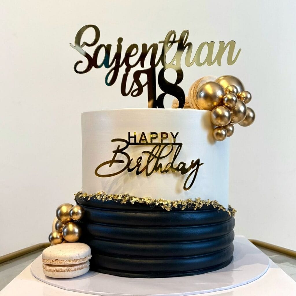 Elegant birthday cake with gold accents and modern topper on black and white icing.