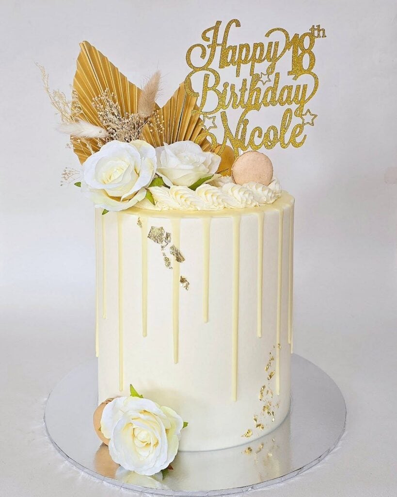 Elegant white birthday cake with gold accents and floral decorations, perfect for celebrations.