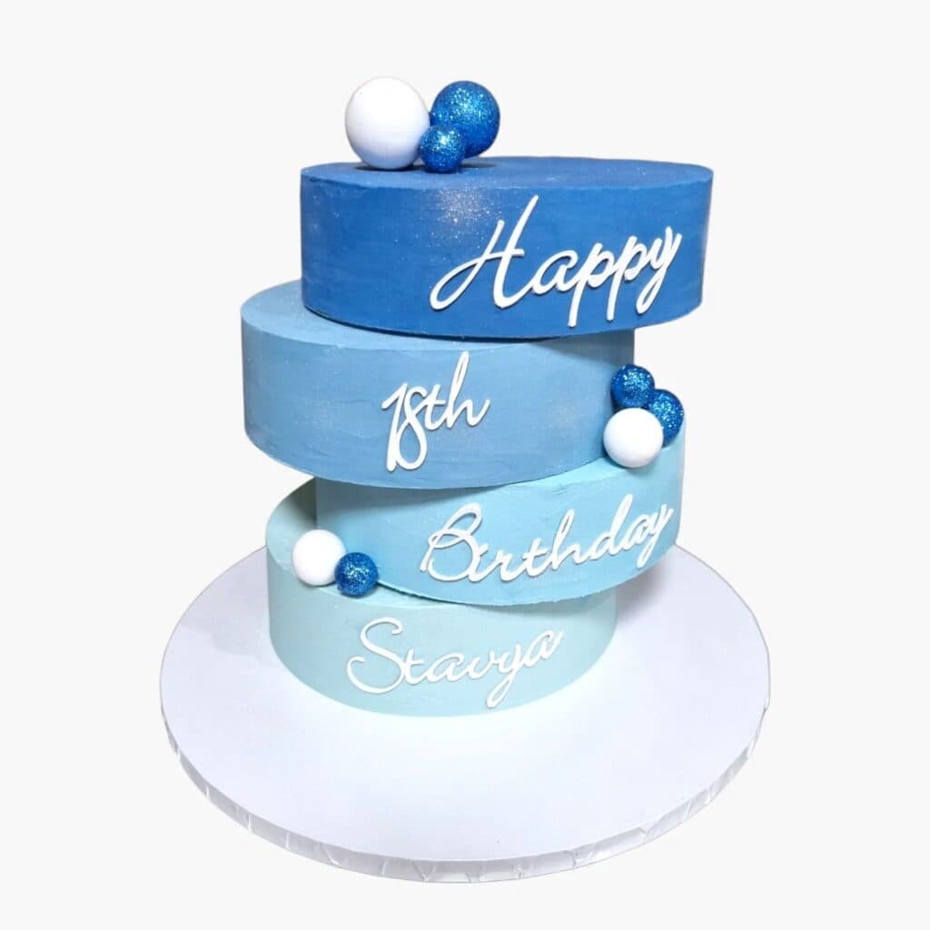 Blue tiered birthday cake with white and blue decorations and "Happy 18th Birthday Starya" written.