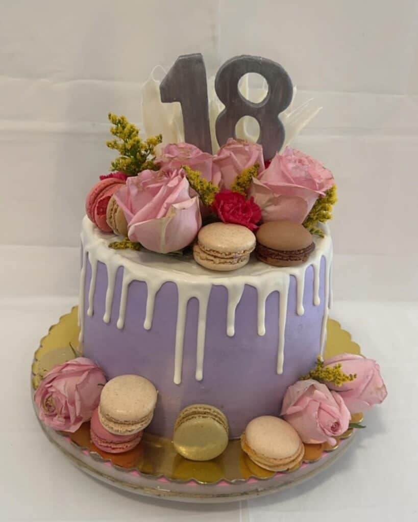 Colorful birthday cake decorated with pink roses, macarons, and number 18 topper, elegant celebration dessert.