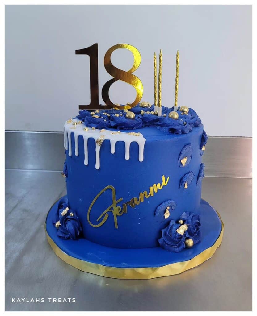 Elegant 18th birthday cake in blue with gold accents and floral decorations.