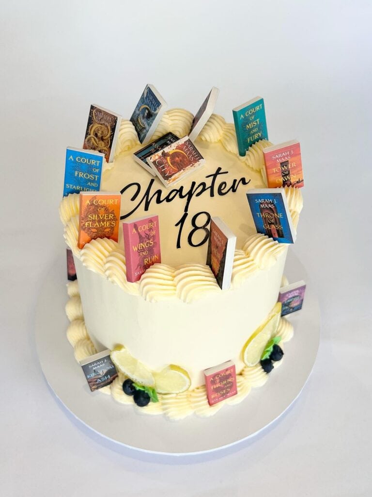 Colorful book-themed birthday cake with "Chapter 18" topper and book figurines, elegant celebration dessert.
