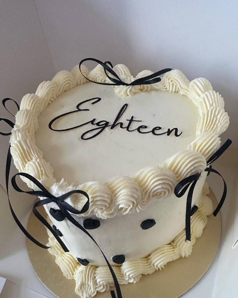 Decorative heart-shaped birthday cake with white frosting and black lettering "Eighteen".