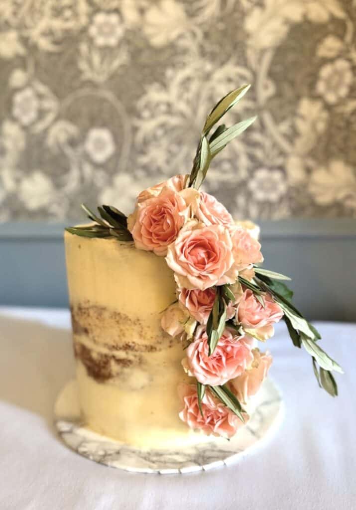 Elegant wedding cake with fresh pink roses and greenery decoration.