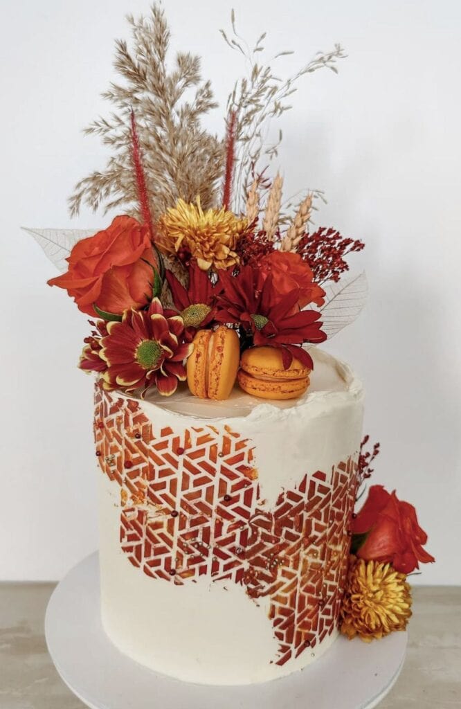 Vibrant autumn-themed floral cake with roses, dahlias, and macarons.