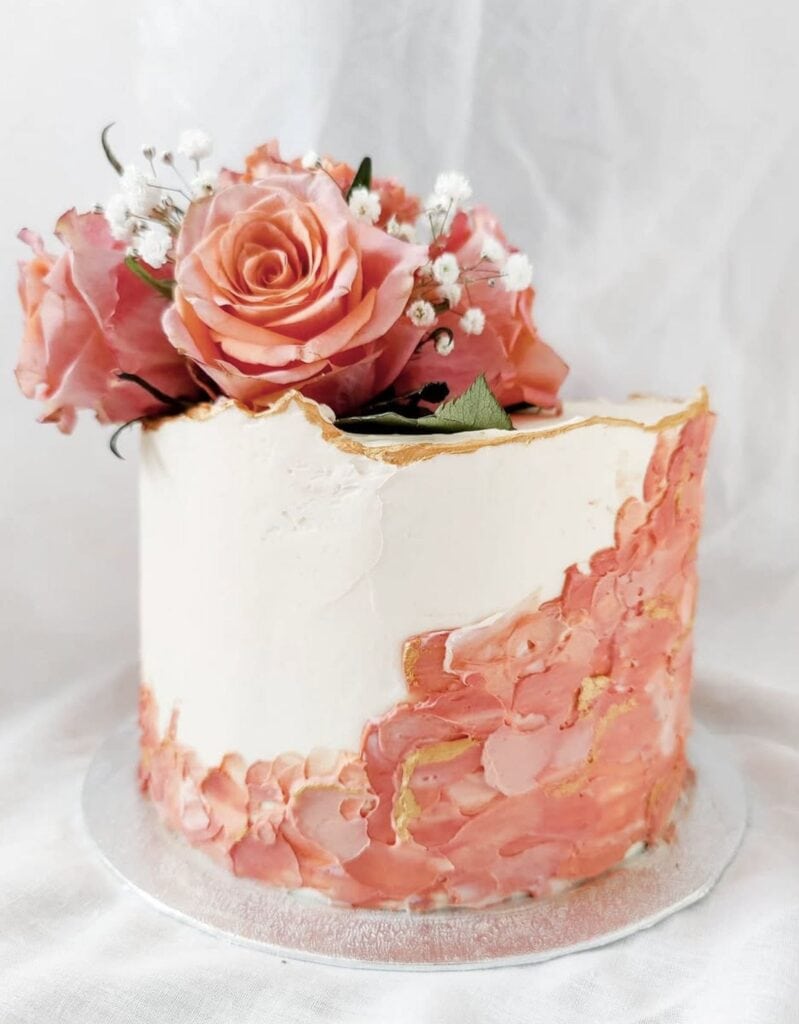 Elegant pink floral cake with roses and gold accents for special occasions.