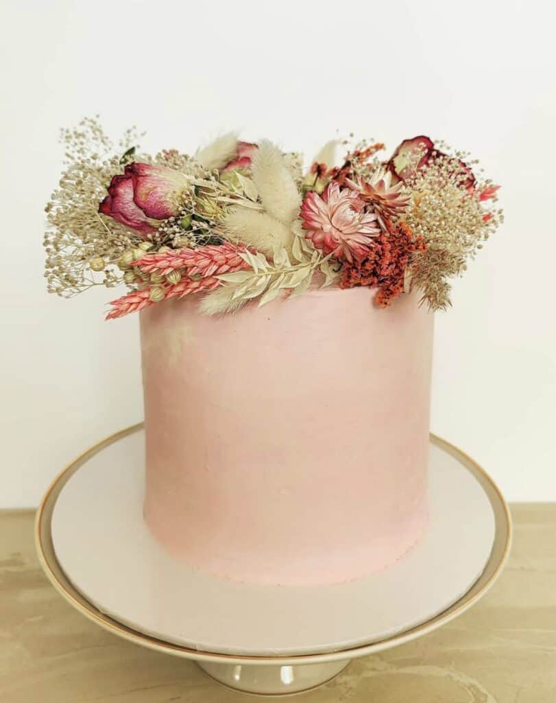 Elegant pink and cream dried flower arrangement in a pastel pink cylindrical vase.