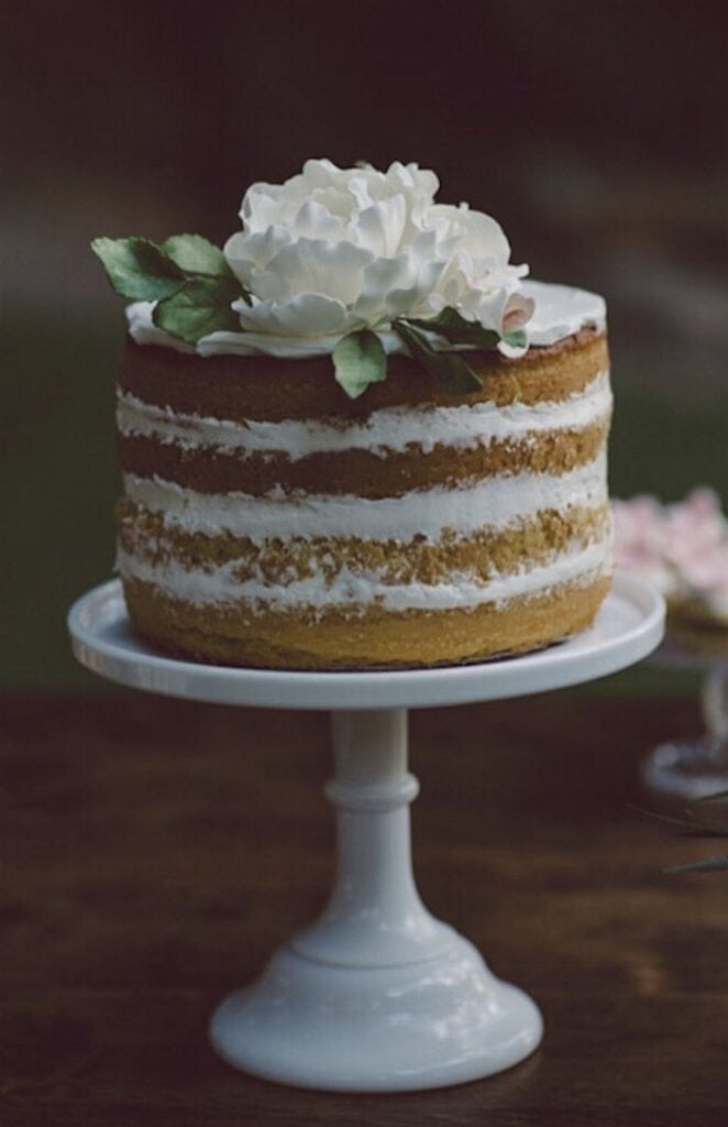 Naked vanilla cake with white flower decoration on cake stand, elegant wedding dessert.