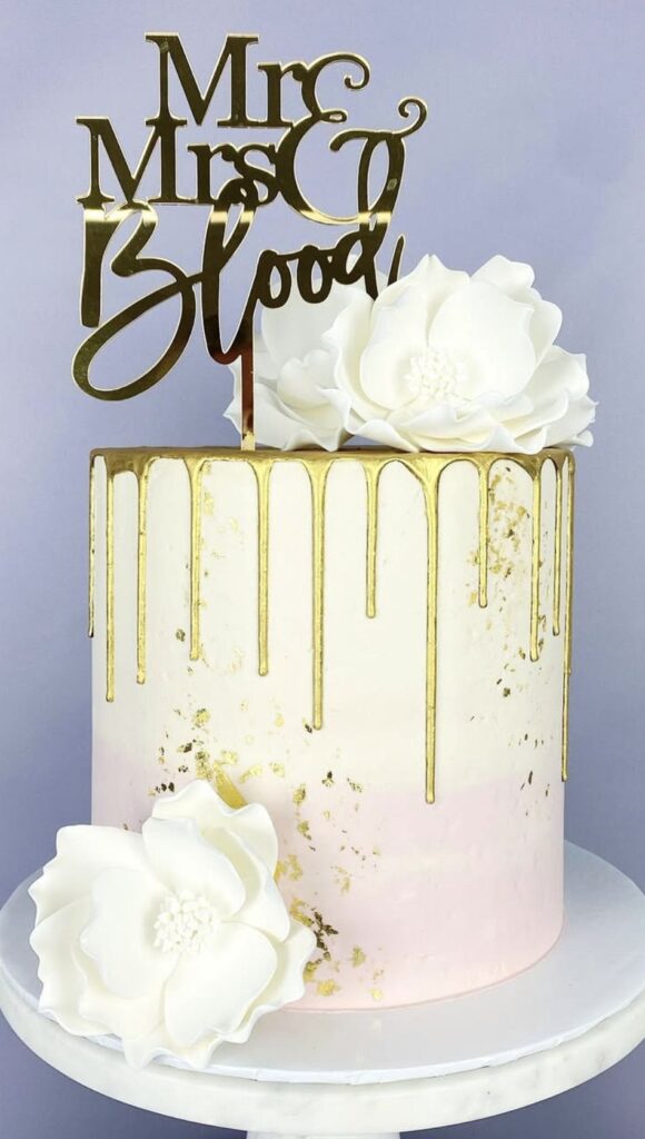 Elegant wedding cake with white flowers and gold drip decoration.