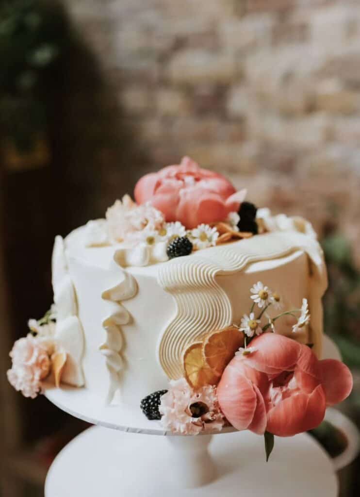 Elegant wedding cake decorated with pink flowers, white icing, and floral accents.