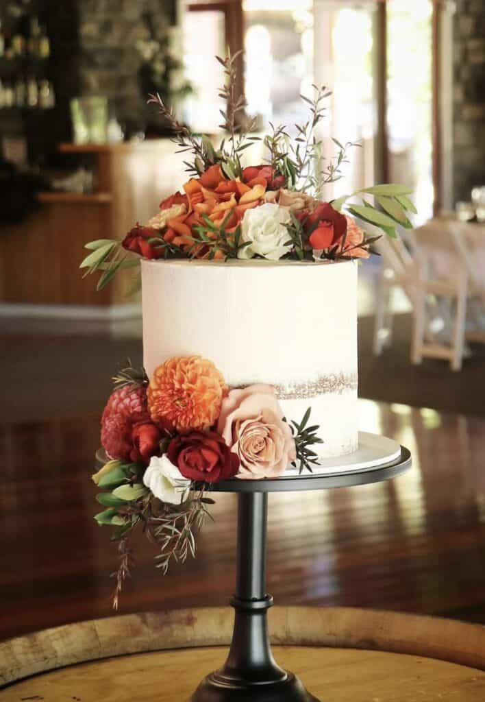 Elegant floral wedding cake with peach, red, and white roses and greenery.