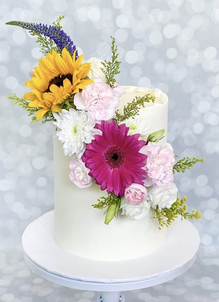Bright floral cake with sunflower, gerbera, roses, and lavender decorations.