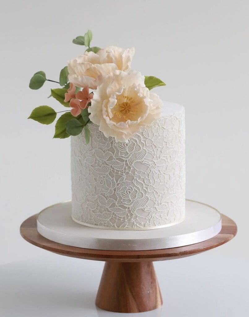 Elegant floral wedding cake with lace detailing and pastel blooms, perfect for special occasions.