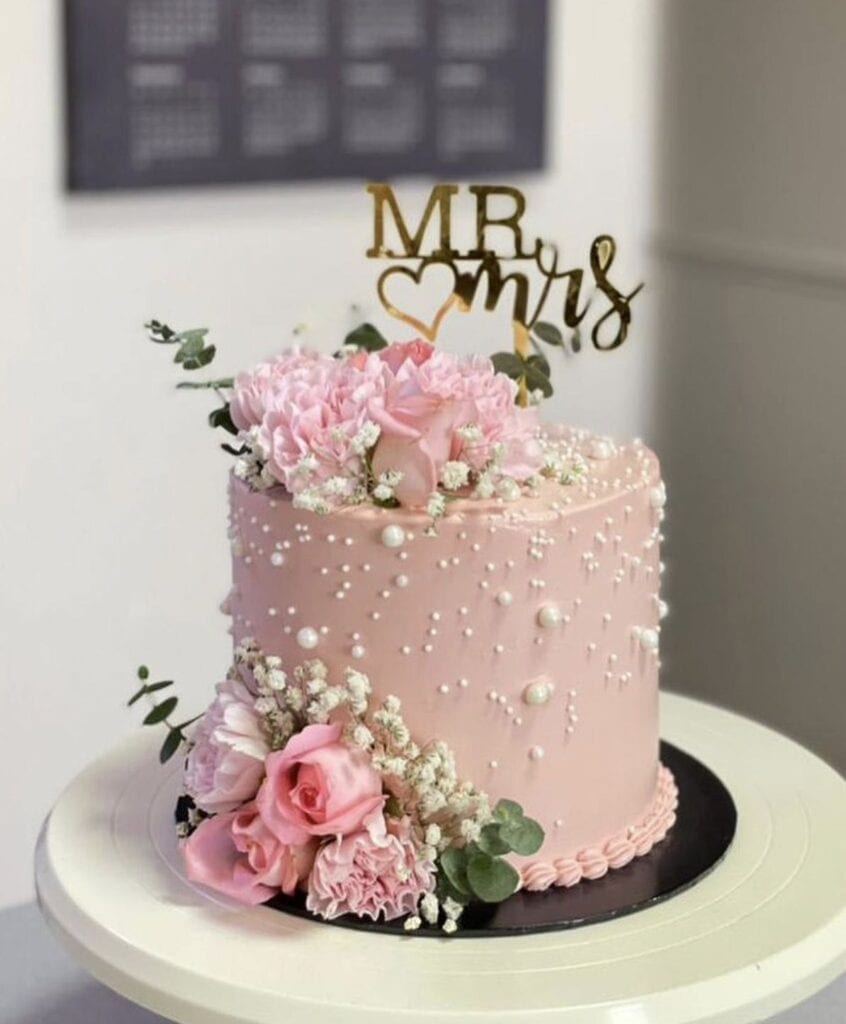 Elegant pink wedding cake with floral decorations and "Mr & Mrs" topper.