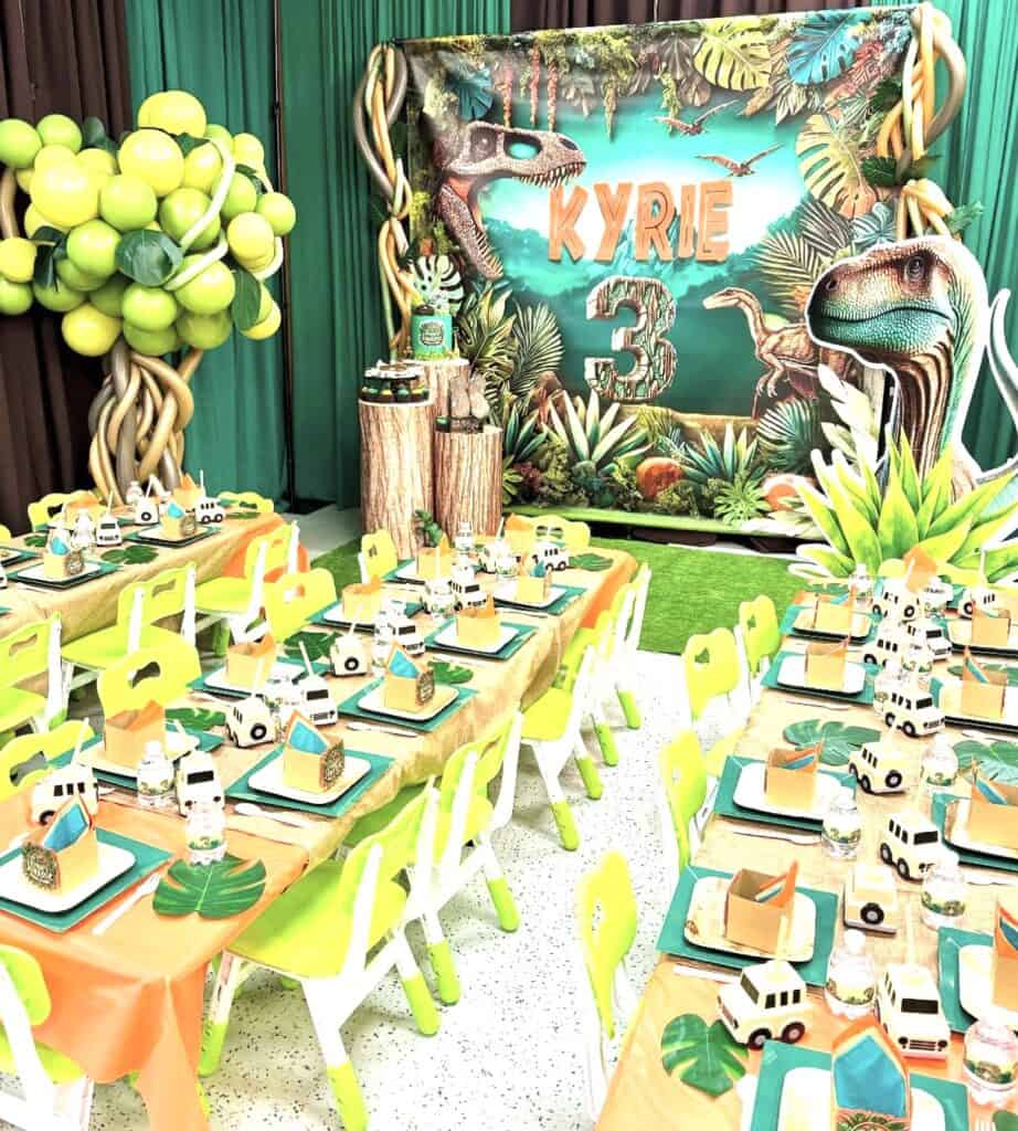 Bright dinosaur-themed birthday party decor with jungle foliage and table settings.