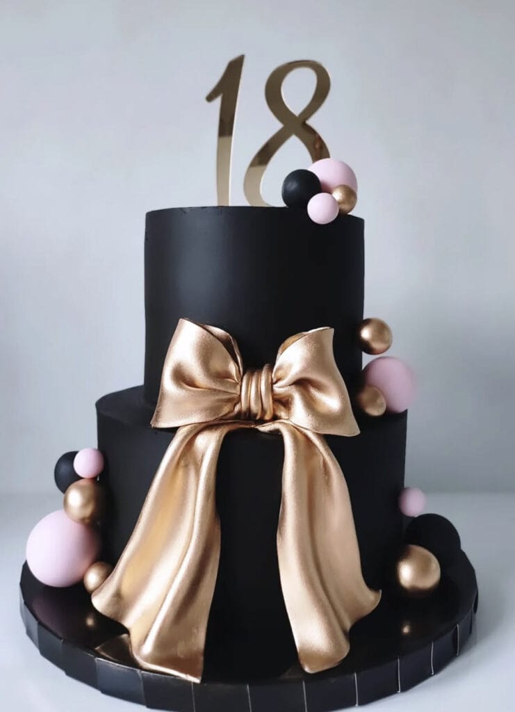 Elegant black birthday cake with gold bow and modern sugar decorations, 18th birthday celebration, luxury dessert design.