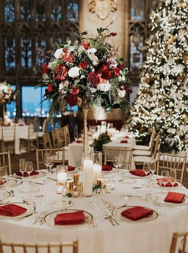 Elegant holiday wedding reception table with floral centerpiece and Christmas tree decor.