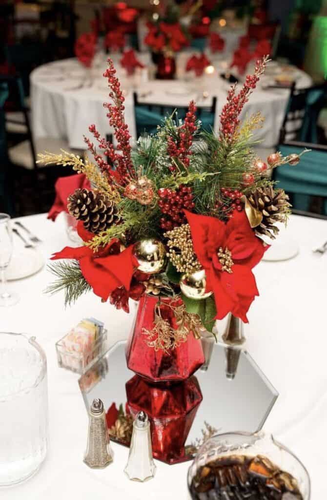 Festive Christmas centerpiece with poinsettias, pinecones, and gold ornaments in a red vase.