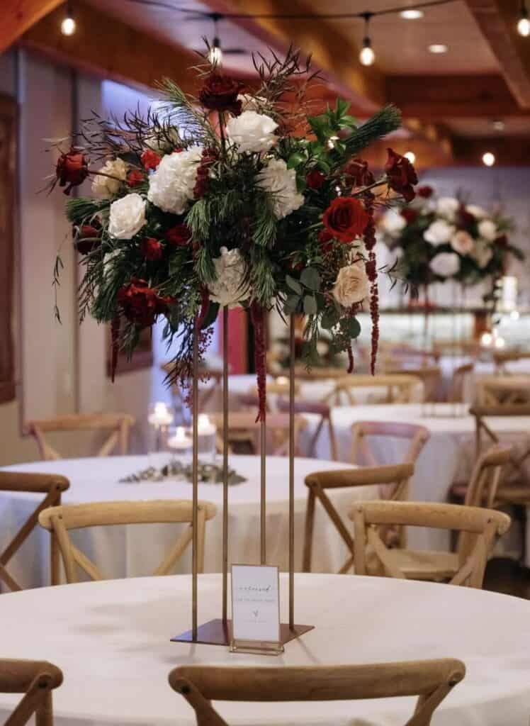 Elegant wedding centerpiece with red and white roses, greenery, and decorative foliage.