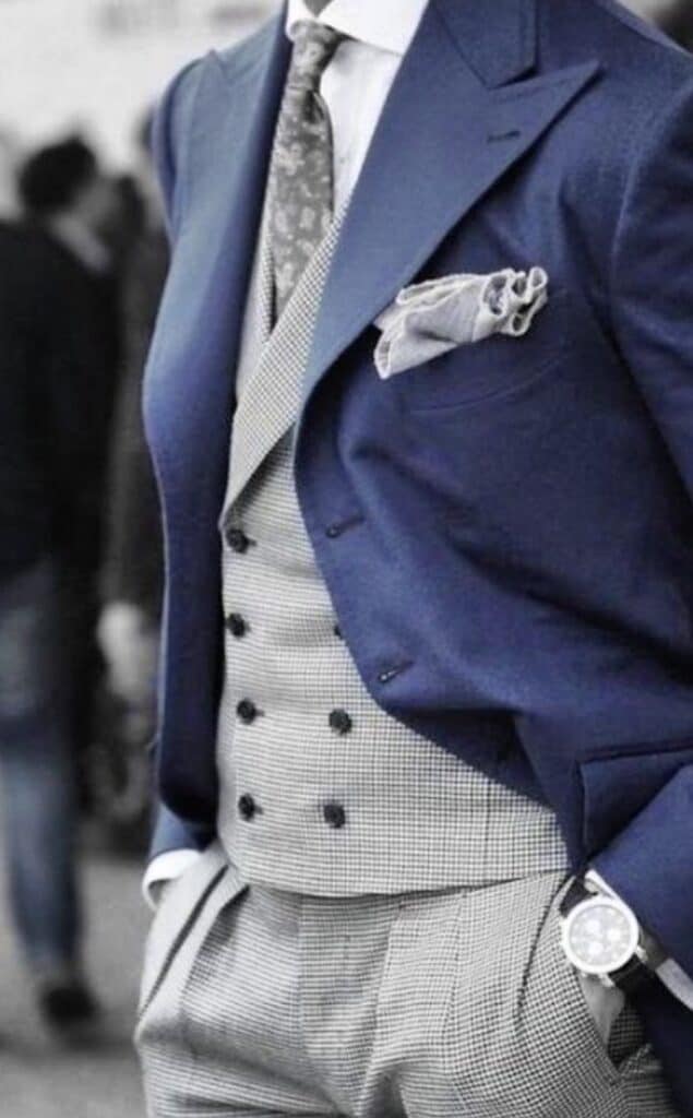 Elegant men's suit with blue blazer, patterned vest, and pocket square.