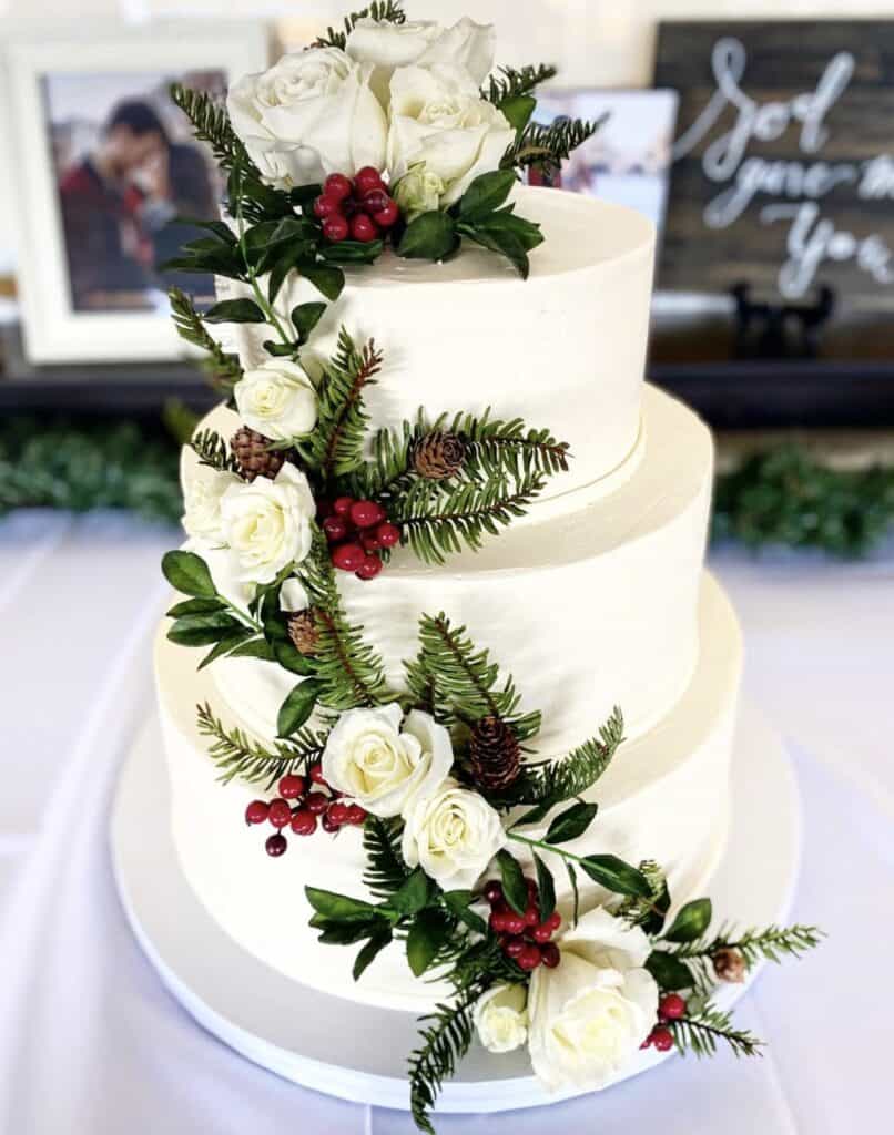 Elegant wedding cake with white roses, greenery, and red berries.