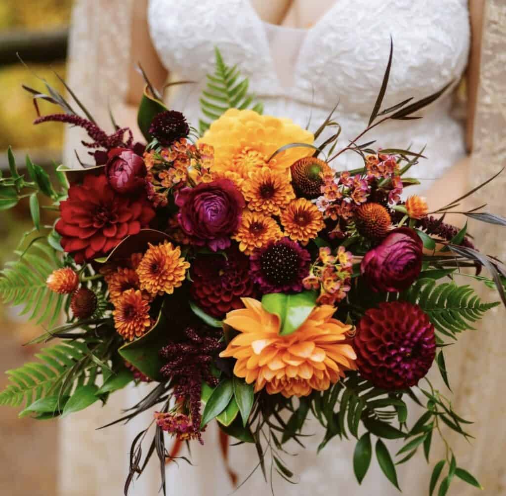Vibrant fall bouquet with orange, red, and burgundy flowers and lush greenery.