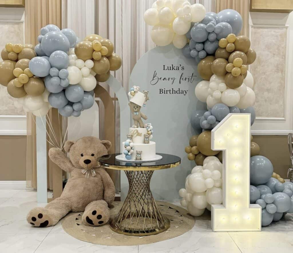 Balloon arch with blue, beige, and white balloons for birthday celebration.