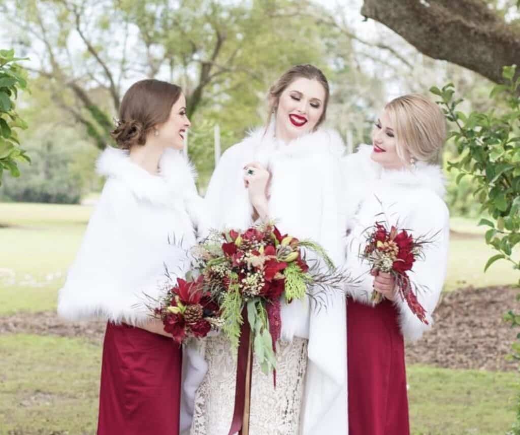 Elegant bridesmaids holding vibrant red floral bouquets outdoors.