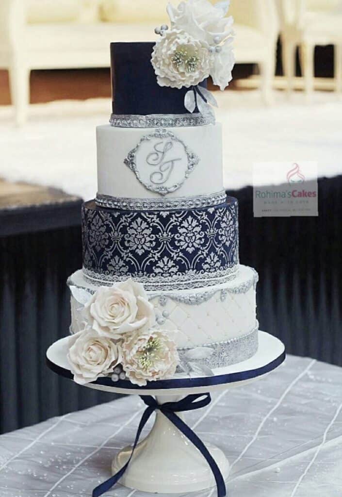 Elegant white and navy wedding cake with lace, floral accents, and monogram topper.