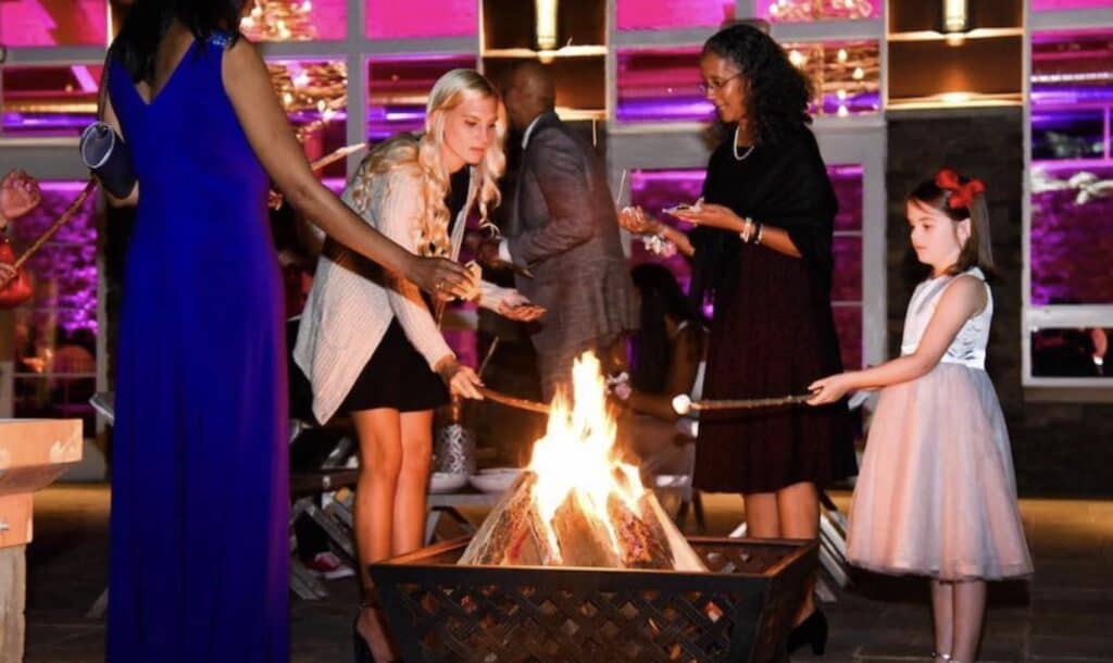 People gathered around a bonfire at a festive celebration, roasting marshmallows.