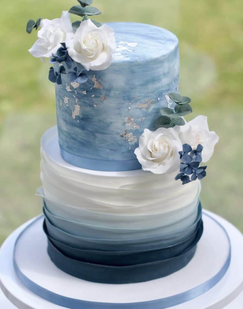 Elegant blue and white wedding cake with floral decorations and gold accents.