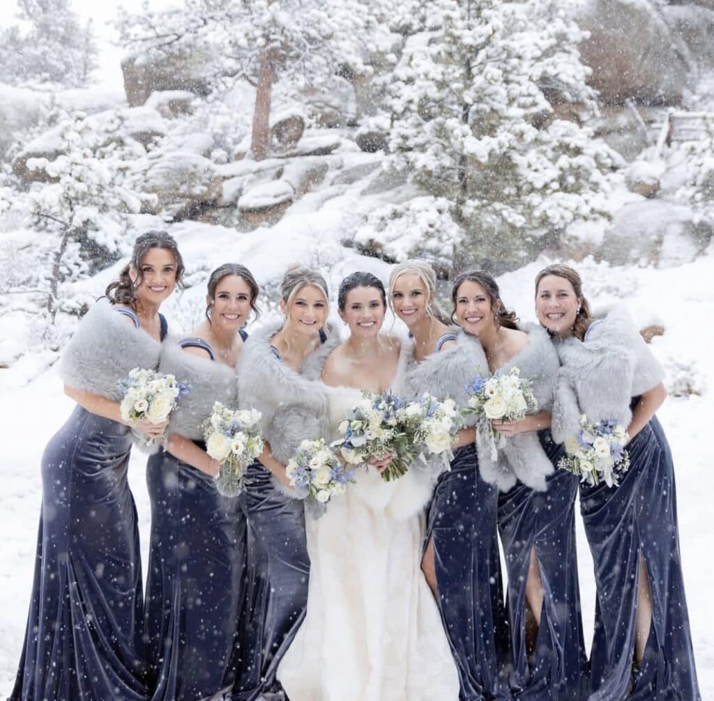 Elegant winter wedding bridal party with floral bouquets in snowy landscape.