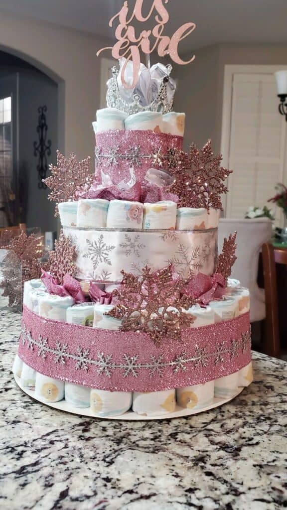 Pink and white diaper cake with glitter snowflakes and "It's a Girl" topper.
