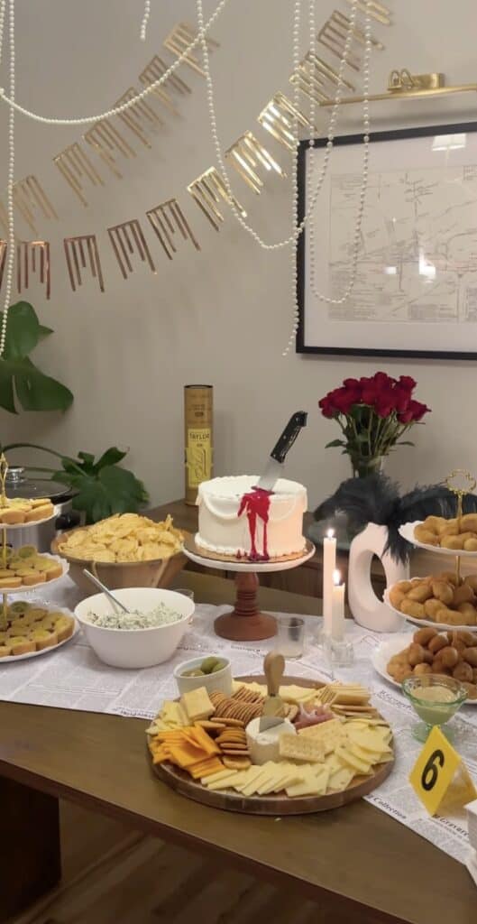 Festive birthday party table with cheese platter, cake, and snacks for celebration.