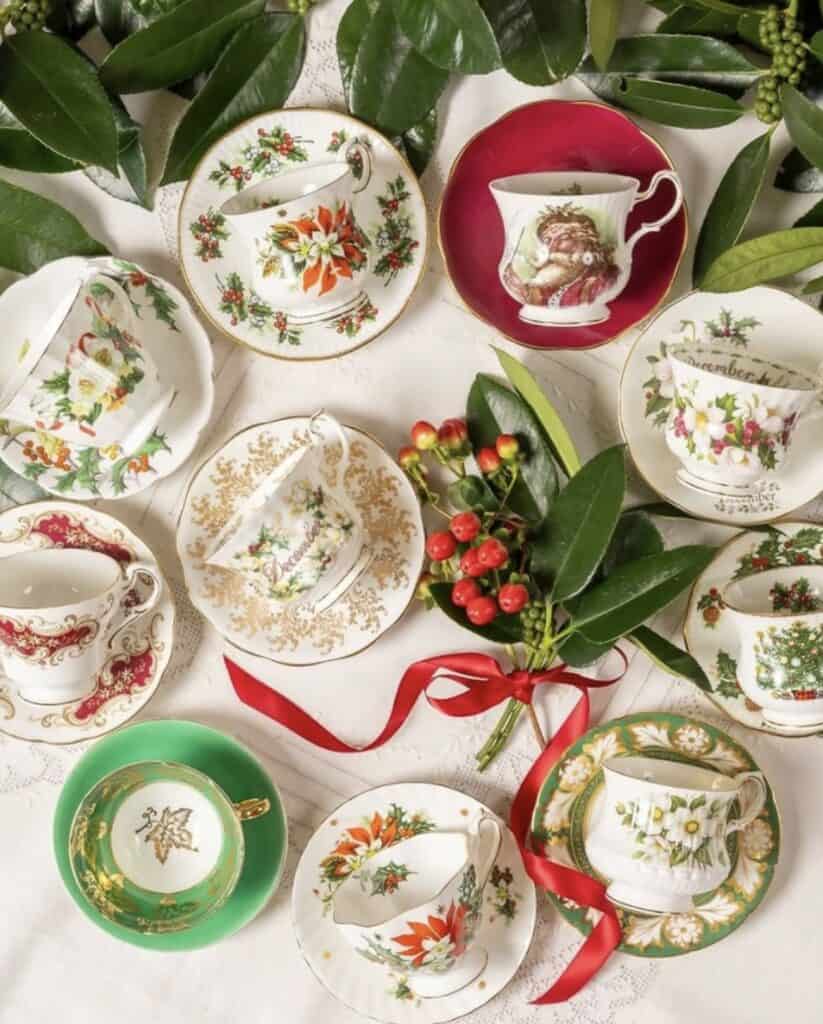 Festive holiday teacups and saucers with Christmas patterns and greenery.