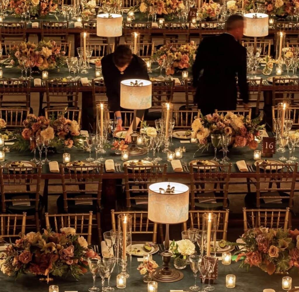 Elegant nighttime event table setup with floral centerpieces and candlelight.
