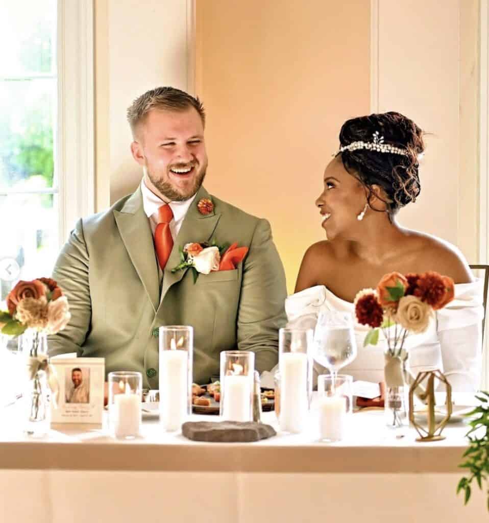 Elegant wedding couple sharing joyful moment at reception table, floral decor and candles.