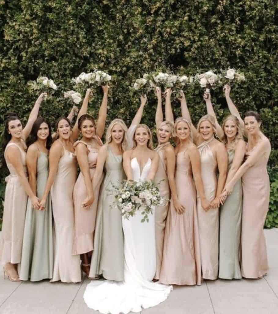 Elegant bridal party with bridesmaids holding bouquets and the bride in a white gown, outdoor setting.